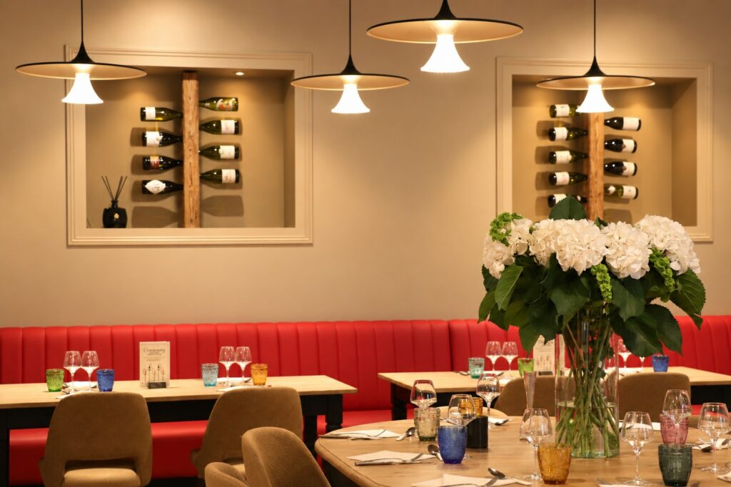 Le Salon : longue banquette rouge, niches de bouteilles au mur, suspensions et bouquet d'hortensias blancs sur une table ronde